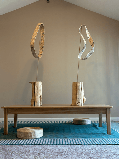 Woven loop sculpture made from rolled paper strips, twisting in a continuous band with multiple rotations, mounted on a weathered wood base with bamboo supports.
