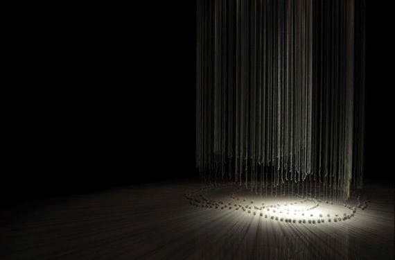 Thread installation suspended above concentric rings of spools in a dark gallery.